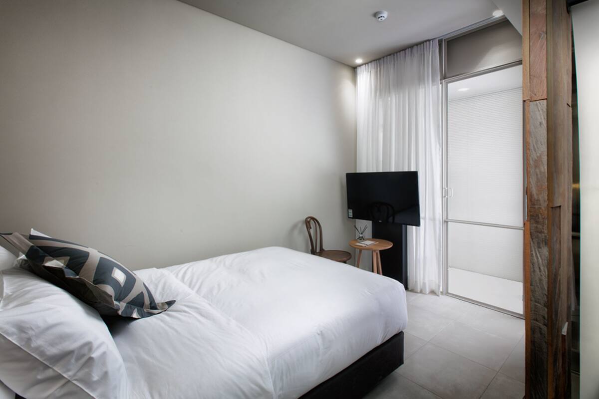 A hotel room with a bed, a TV, a small table, and a chair.