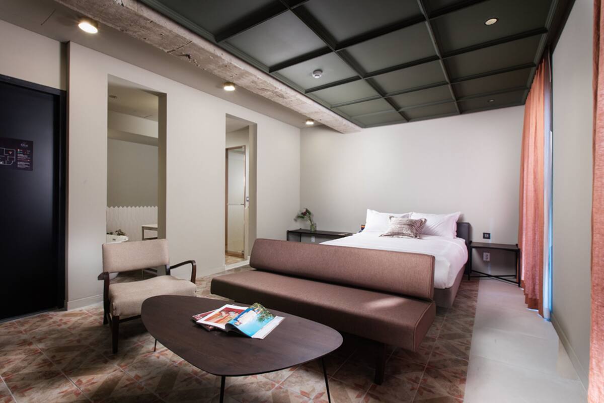 A modern hotel room with a large bed, a sofa, a small table, and a chair.
