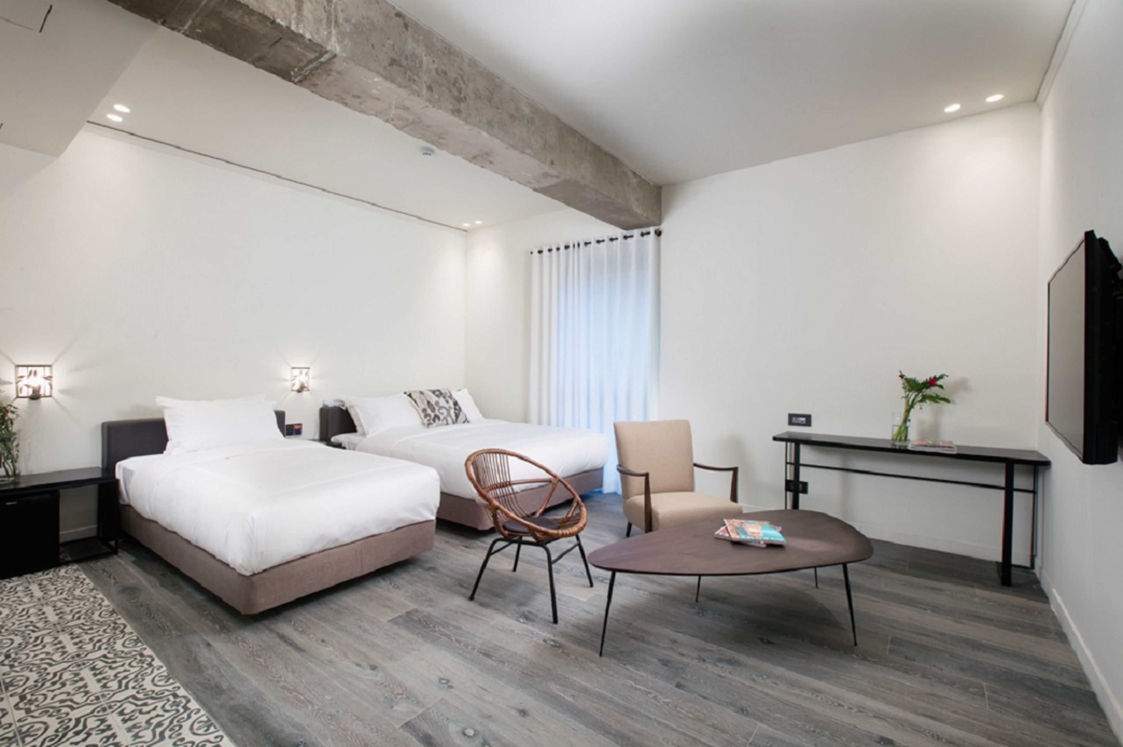 Moderni hotellihuone, jossa on kaksi sänkyä, ruokapöytä, tuoli ja pieni työpöytä.