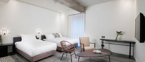 A modern hotel room with two beds, a dining table, a chair, and a small desk.