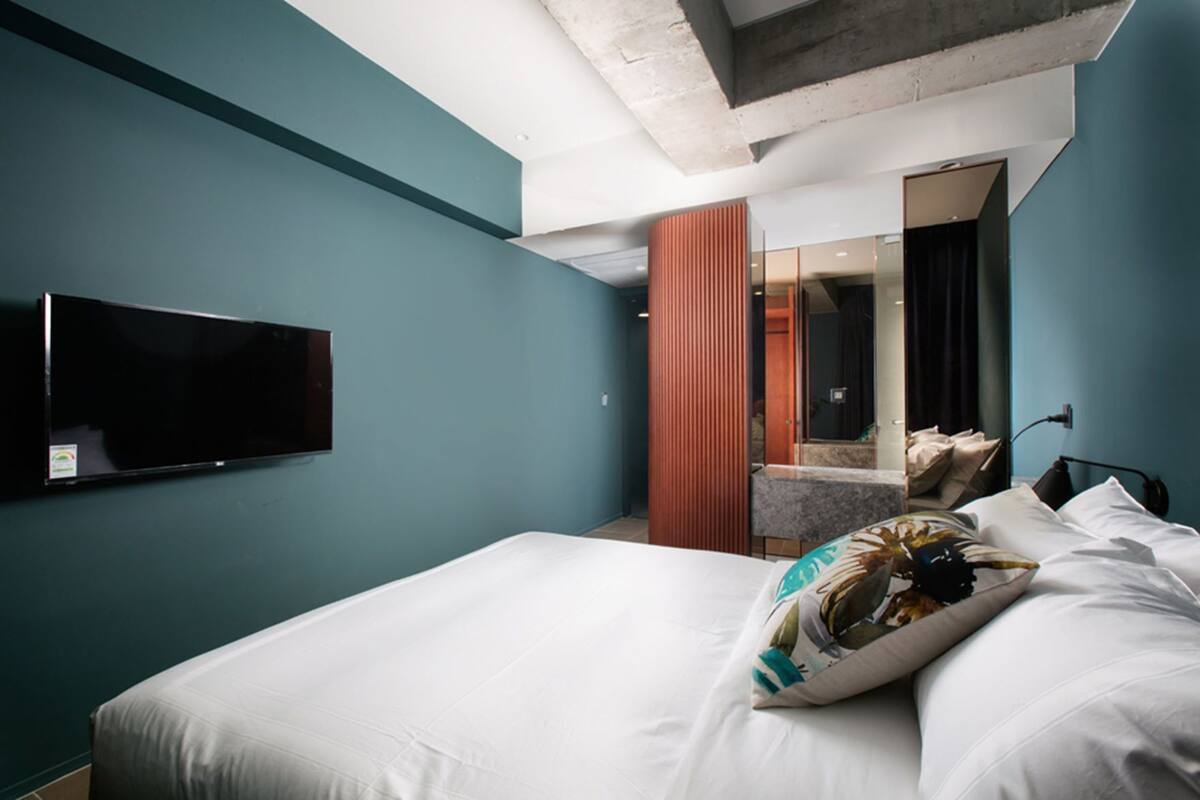 A hotel room with a bed, a TV mounted on the wall, and a bathroom visible through an open door.