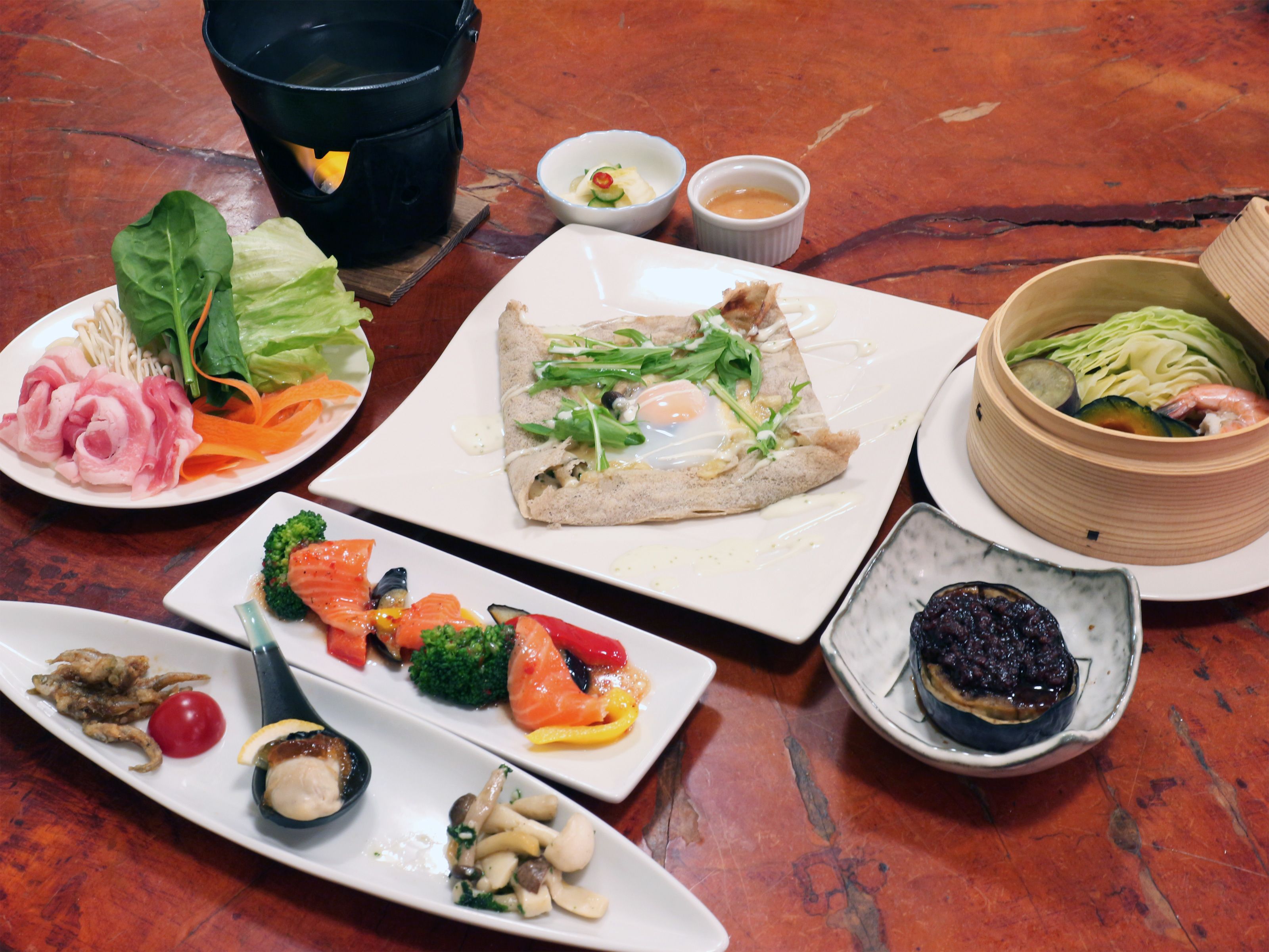 A variety of dishes on a table, including sushi, vegetables, and a bowl of soup.