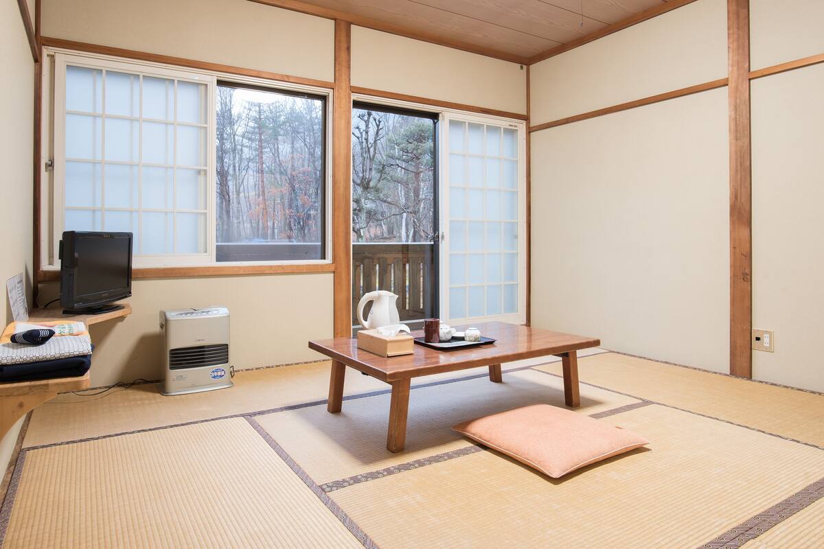 A traditional Japanese room with tatami flooring, a low wooden table, a television, and a heater.