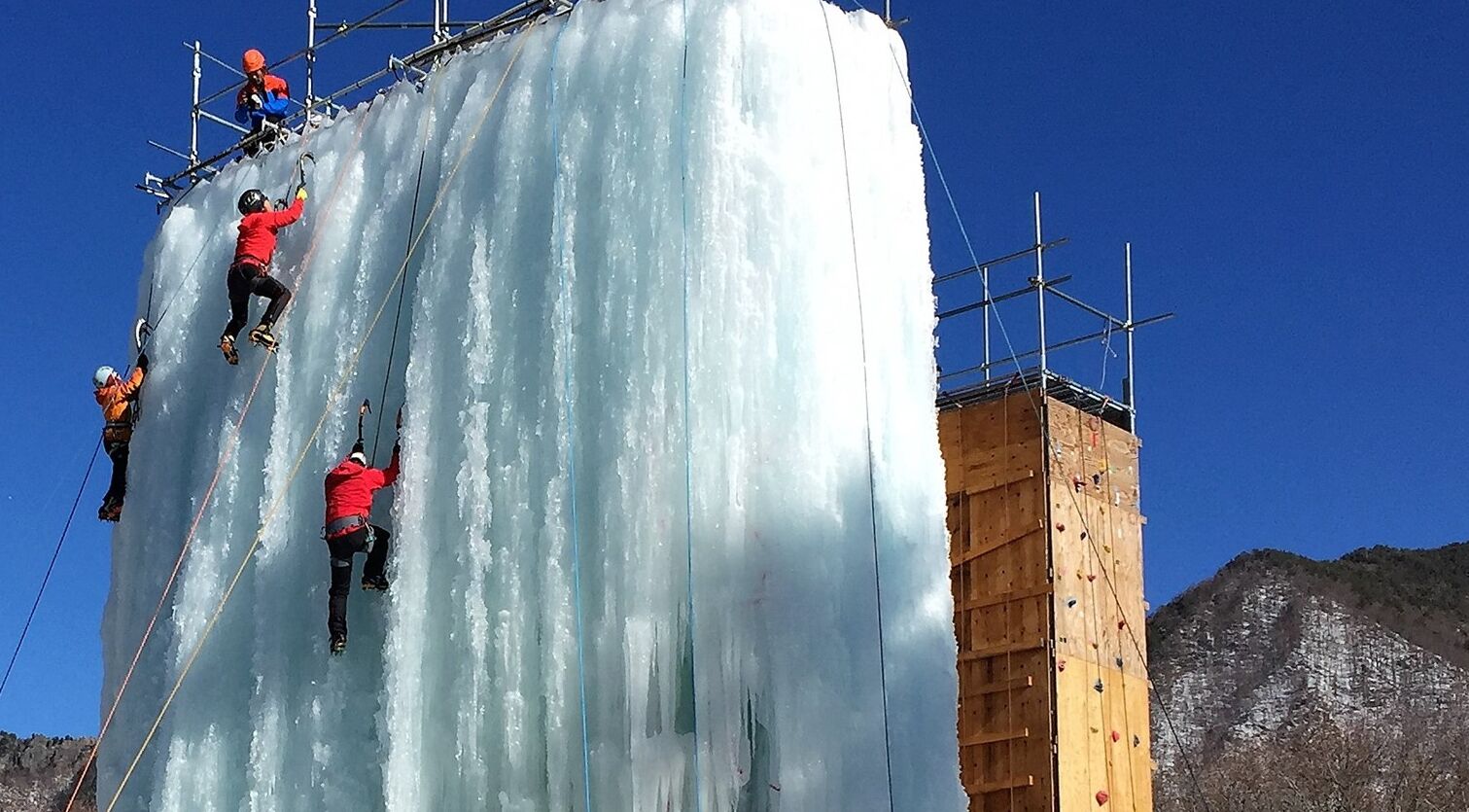 Climbers scaling a large ice wall with wooden scaffolding and metal safety structures.