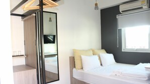 A modern hotel room with a bed, a wooden headboard, a large mirror, a wardrobe, a TV, and an air conditioning unit. - Jam Hostel Bangkok (Bangkok)