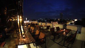 An outdoor seating area with tables and chairs, a view of the cityscape, and a building with a balcony. - Jam Hostel Bangkok (Bangkok)