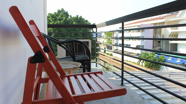 Ein Balkon mit rotem Stuhl und kleinem Tisch, mit Blick auf einen Kanal und Gebäude.