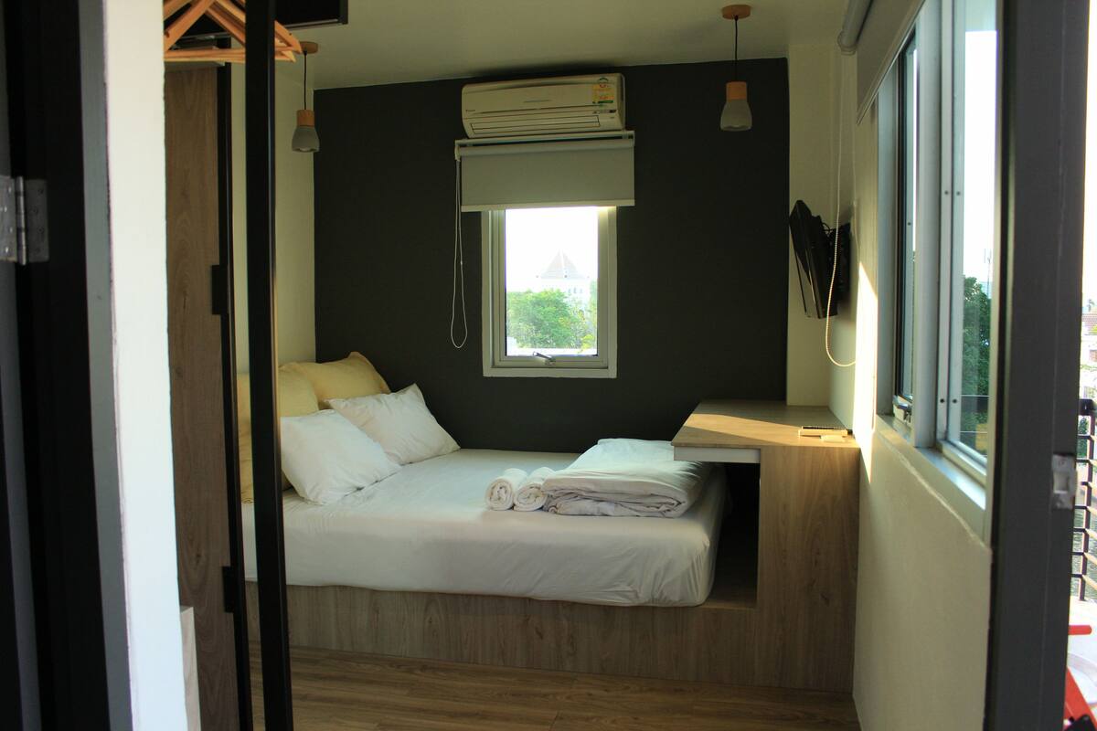 A compact room with a bed, a window, and an air conditioning unit.