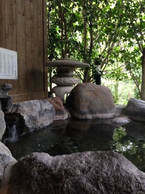 Un jardín japonés tradicional con un farol de piedra, un pequeño estanque y una estructura de madera con un cartel.