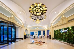A spacious hotel lobby with a large chandelier, seating area, and a green wall with a neon sign.