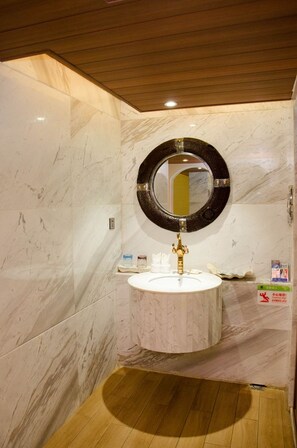 A bathroom with a marble wall, a wooden floor, a round mirror, and a white sink. - Haikou Huangma Holiday Hotel (Haikou)