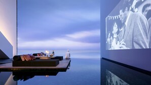 Une piscine à débordement paisible, dotée d’un espace détente avec des coussins et une petite table sur laquelle sont posées des bouteilles.