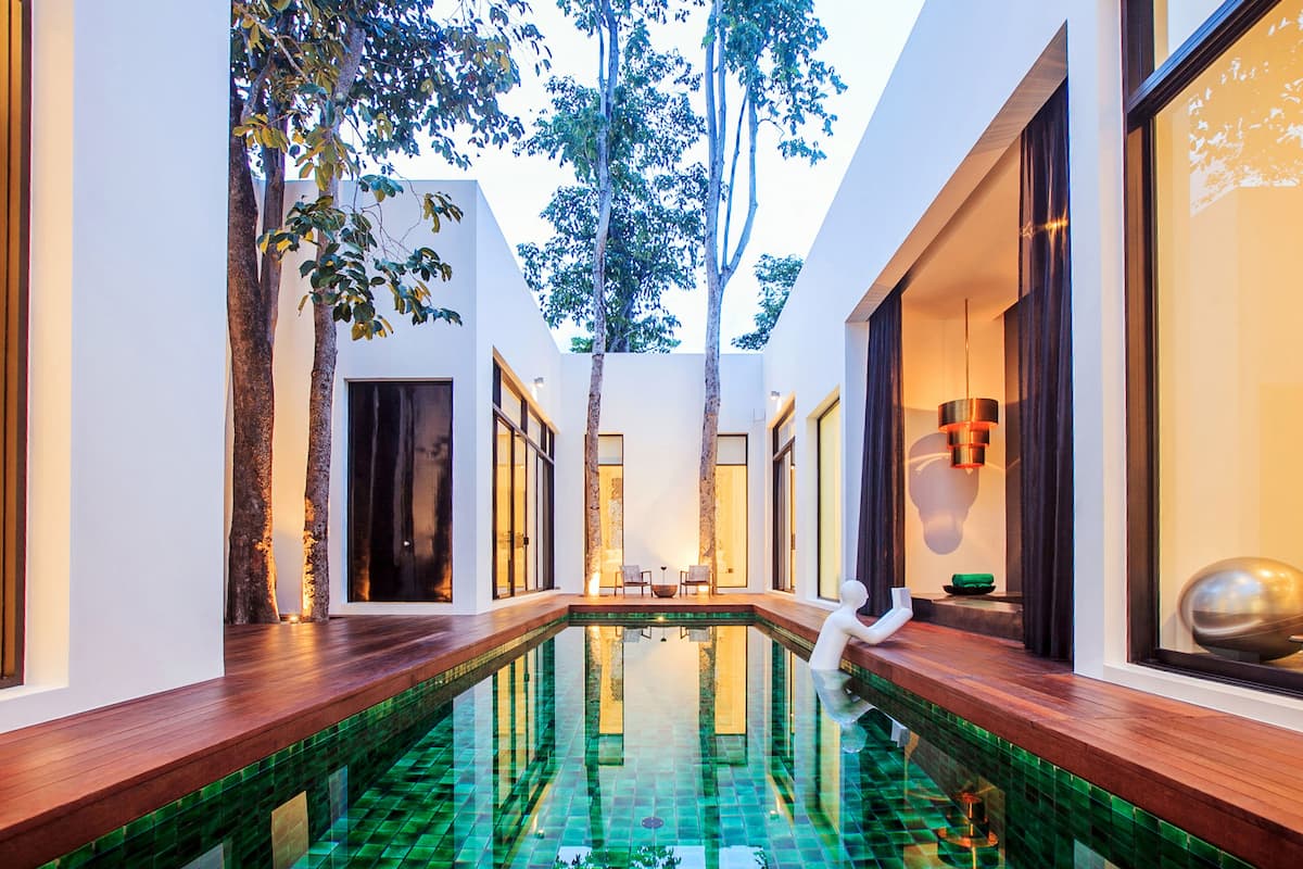 A modern indoor pool with a clear glass bottom, surrounded by wooden decks and white walls.