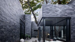 Une terrasse extérieure moderne avec des murs en pierre, une structure vitrée et du mobilier d’extérieur.