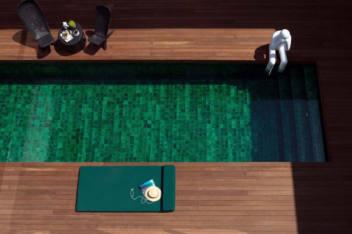 A top-down view of a swimming pool with a wooden deck, two lounge chairs, a small table with a plant, and a sun lounger.