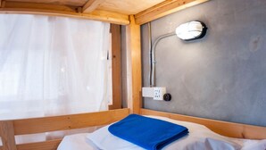A single bed with a blue towel, a wooden headboard, a shower head, and a power outlet on the wall. - A'stel Bangrak - Adults Only - Hostel (Bangkok)