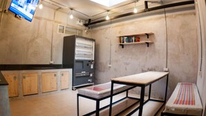 A kitchen with a large refrigerator, wooden cabinets, a wooden table, and a shelf with books. - A'stel Bangrak - Adults Only - Hostel (Bangkok)