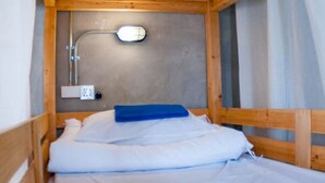 A small, wooden bunk bed with a single bed at the bottom and a bunk above. There is a wall-mounted light fixture and a power outlet on the wall. - A'stel Bangrak - Adults Only - Hostel (Bangkok)