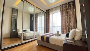 A modern hotel room with a large mirror, a bed with a striped bedspread, a bedside table, and a view of the city through large windows. - Dorsett Residences Bukit Bintang by De Space (Kuala Lumpur)