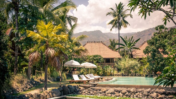 A pool area with lounge chairs and umbrellas, surrounded by palm trees and a mountain backdrop. - Desa Saya Eco Luxury Resort & Spa (Tejakula)