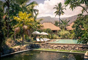 A pool area with lounge chairs and umbrellas, surrounded by palm trees and a mountain backdrop. - Desa Saya Eco Luxury Resort & Spa (Tejakula)