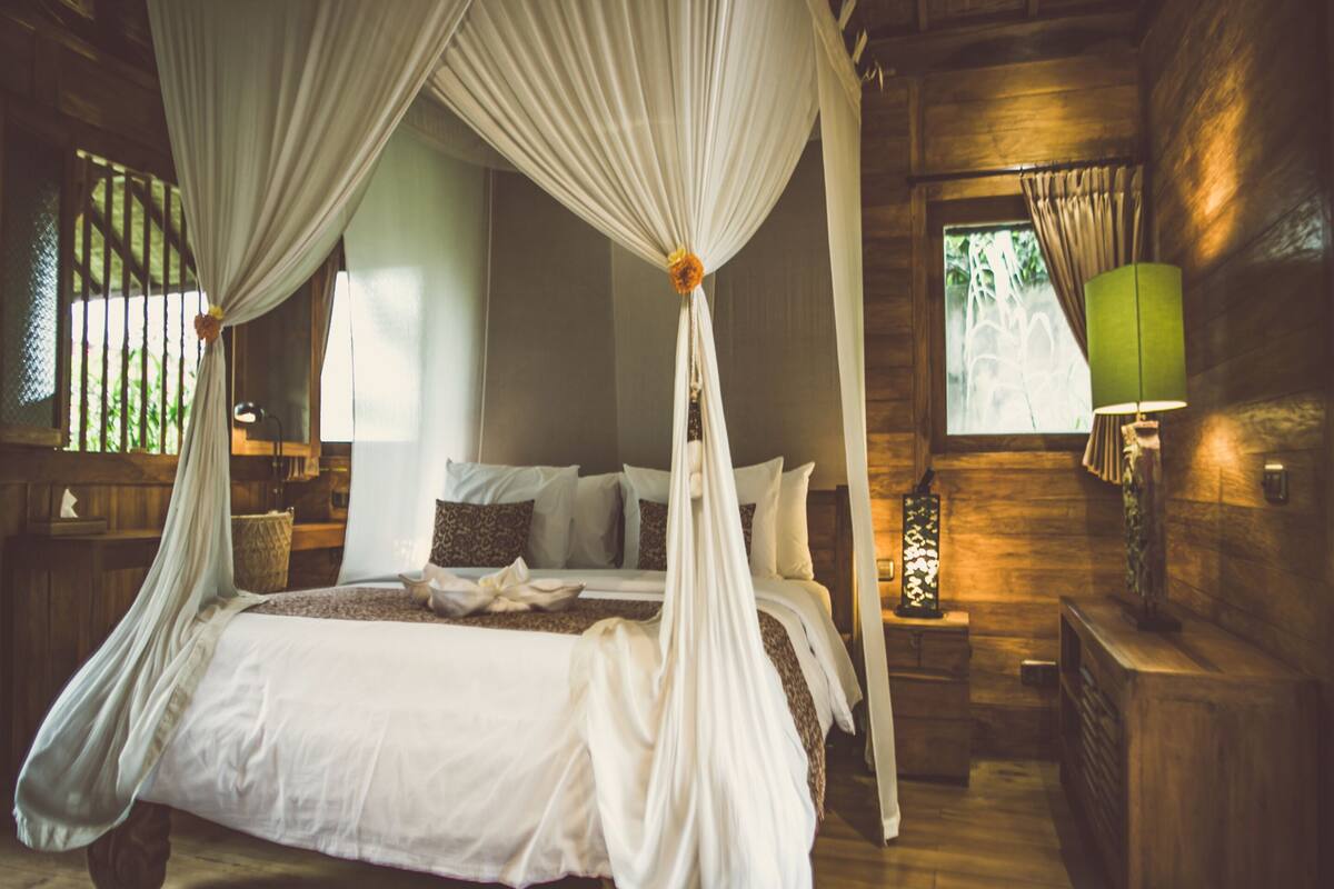 Un lit à baldaquin à quatre poteaux, avec un couvre-lit blanc, une tête de lit en bois et des tables de chevet avec des lampes.