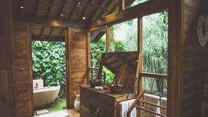 A rustic wooden bathroom with a freestanding bathtub, wooden cabinets, and a large window offering a view of greenery. - Desa Saya Eco Luxury Resort & Spa (Tejakula)