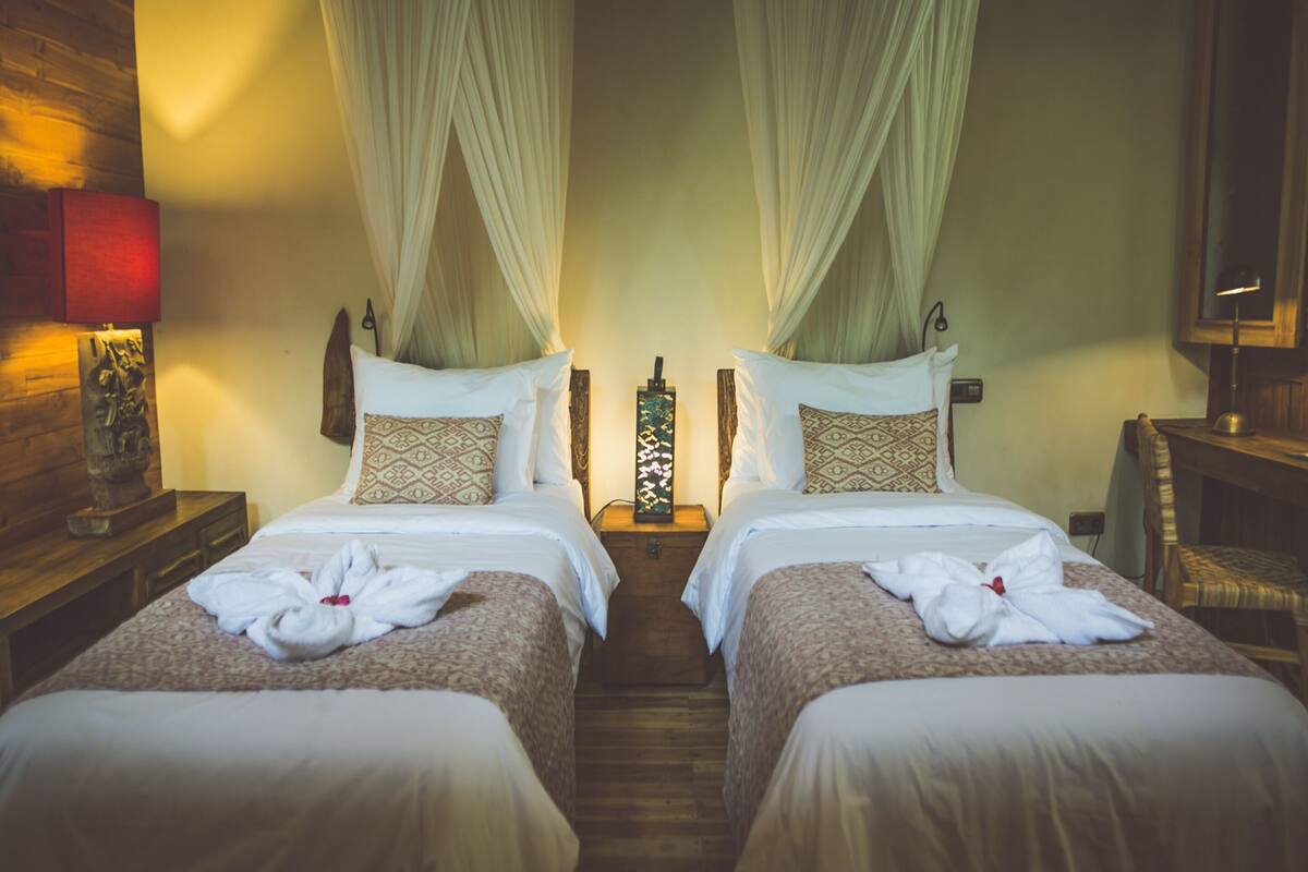 Une chambre d’hôtel avec deux lits, chacun doté d’un baldaquin, d’une table de chevet avec une lampe et d’une tête de lit en bois.