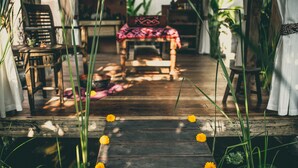 A wooden deck with a rustic chair and a table, surrounded by greenery and flowers. - Desa Saya Eco Luxury Resort & Spa (Tejakula)