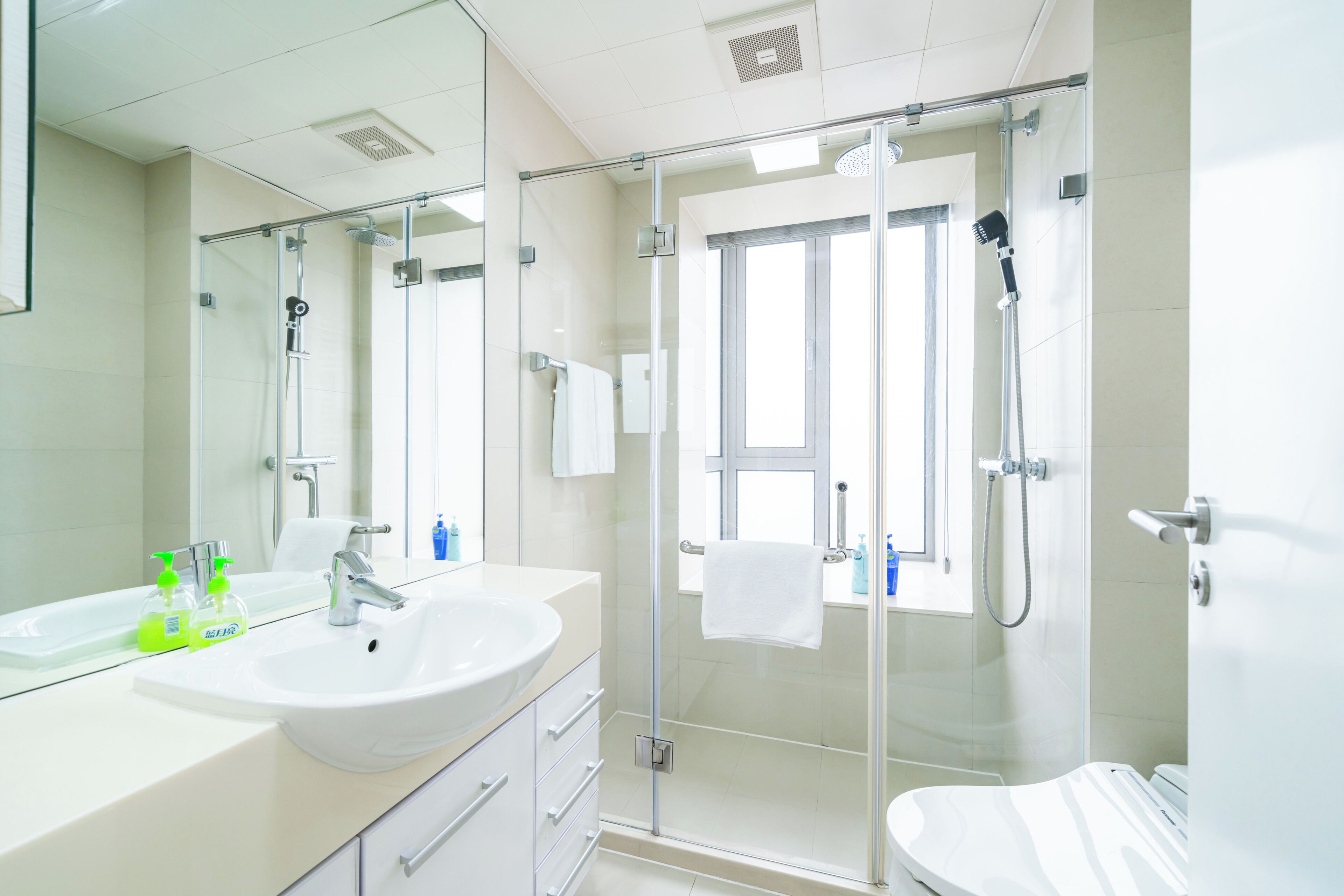 A modern bathroom with a glass-enclosed shower, a large mirror, and a white sink.