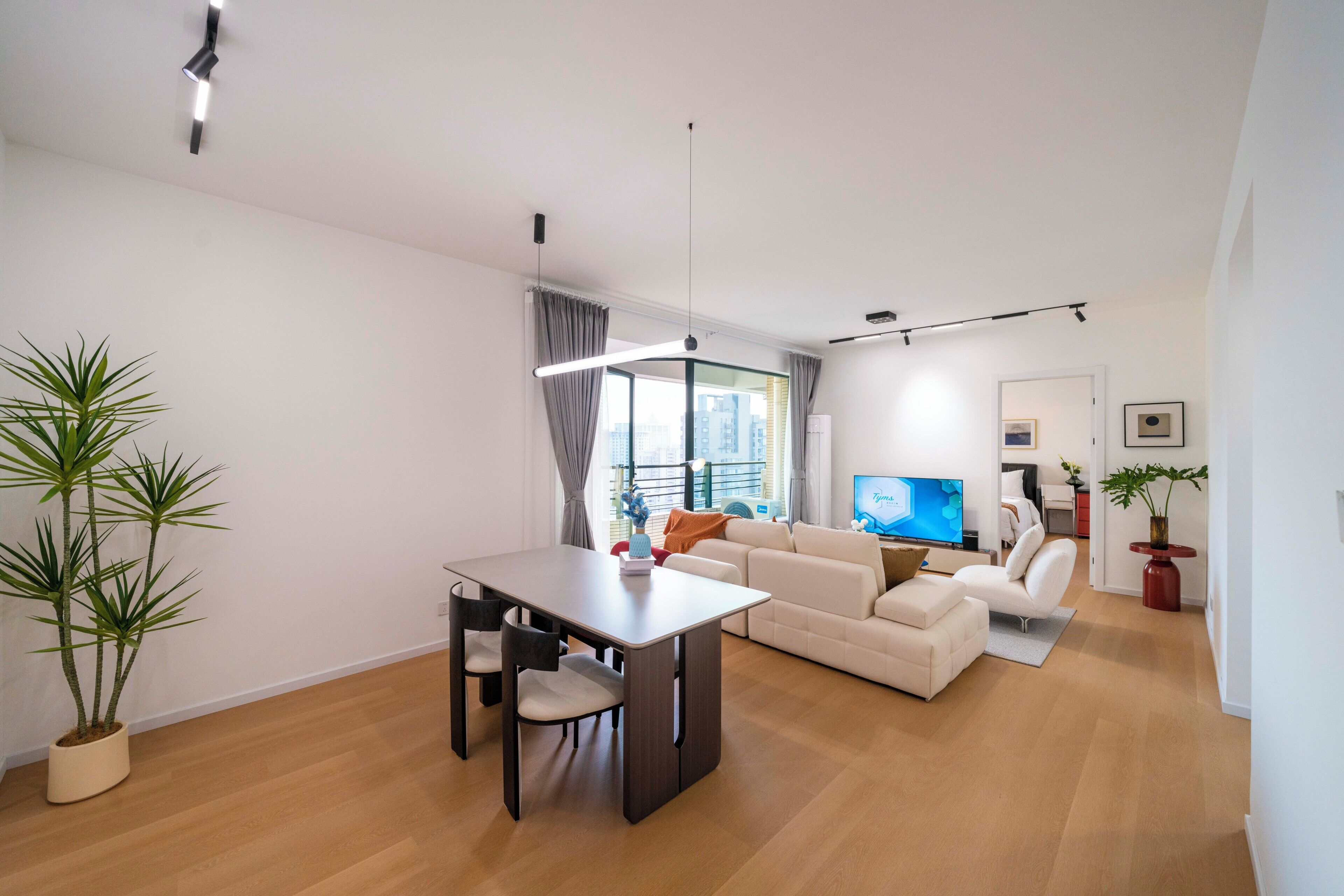 A modern living room with a dining area, a sofa set, a flat-screen TV, and a potted plant.