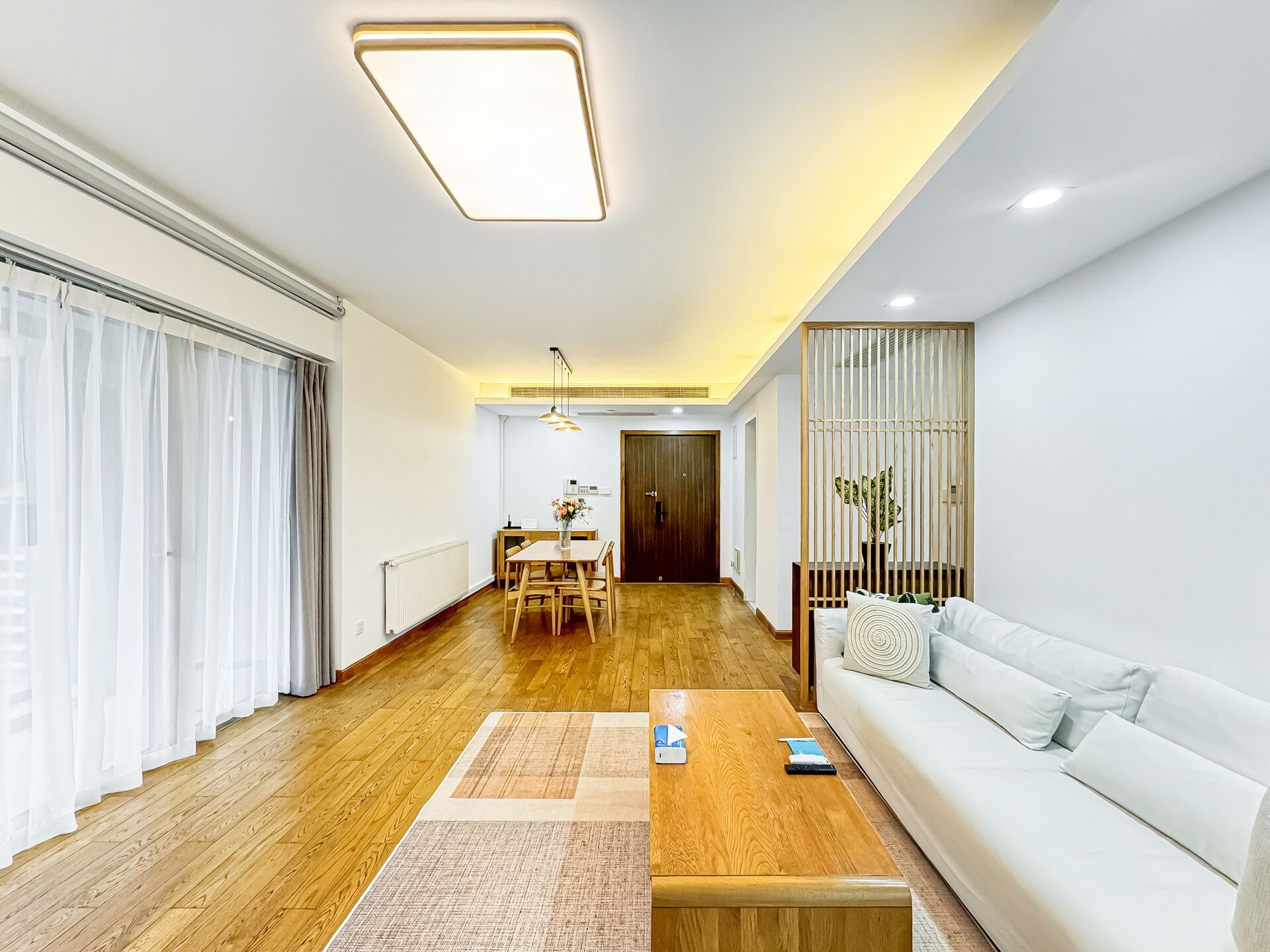 A modern living room with a wooden floor, white sofa, and a dining area with a wooden table and chairs.