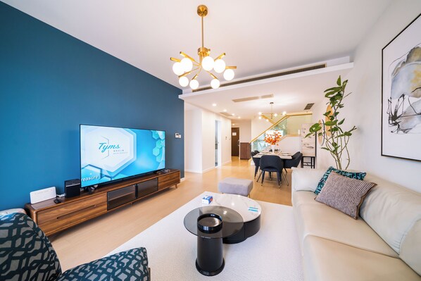 Una sala moderna con televisor de pantalla plana, un sofá, una mesa de centro y un comedor al fondo.