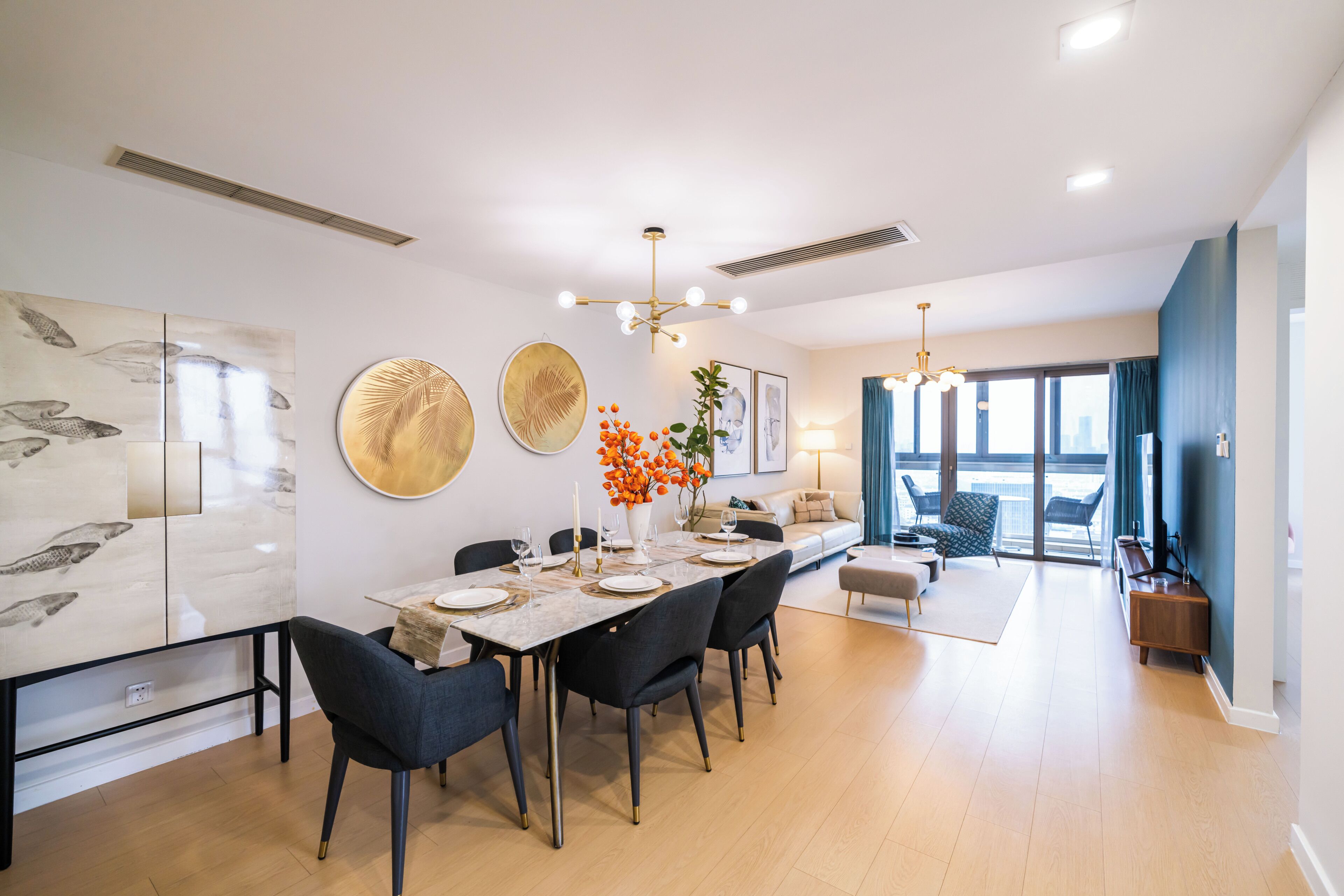 A modern dining area with a long table, chairs, and a vase of flowers.