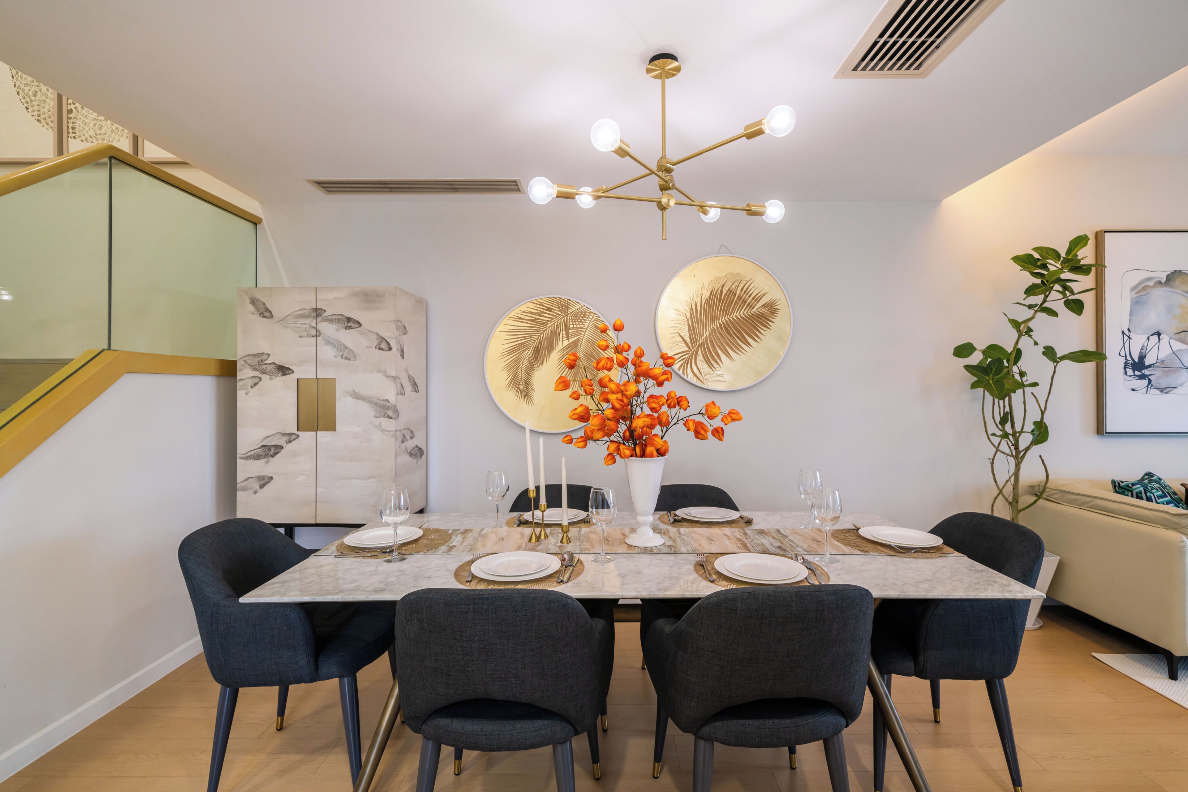 Un comedor con una mesa de mármol, seis sillas, una lámpara de araña y obras de arte en la pared.