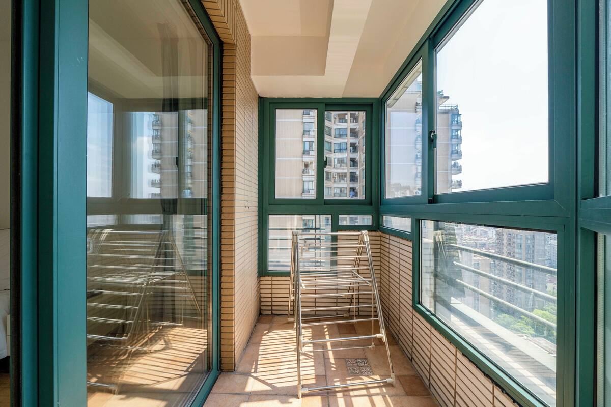 A corner balcony with a metal drying rack, large windows, and a view of high-rise buildings.