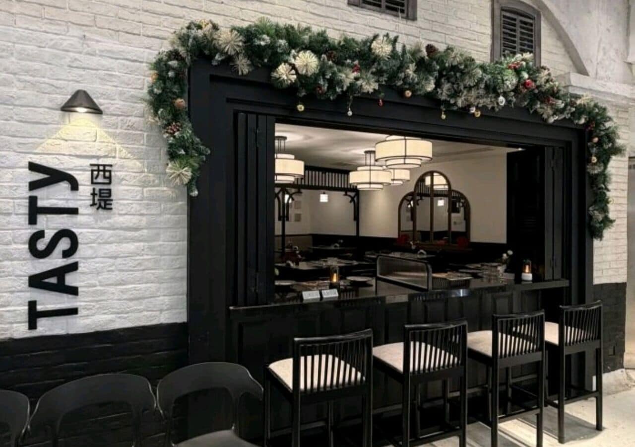 Een restaurant met een zwart uiterlijk en een witte bakstenen muur, met een bord waarop 'TASTY' staat.