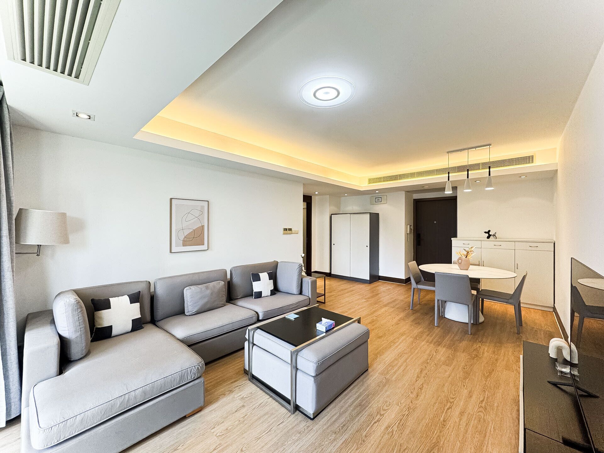 Un salon moderne avec un canapé gris, une table basse et un coin repas comprenant une table et des chaises.