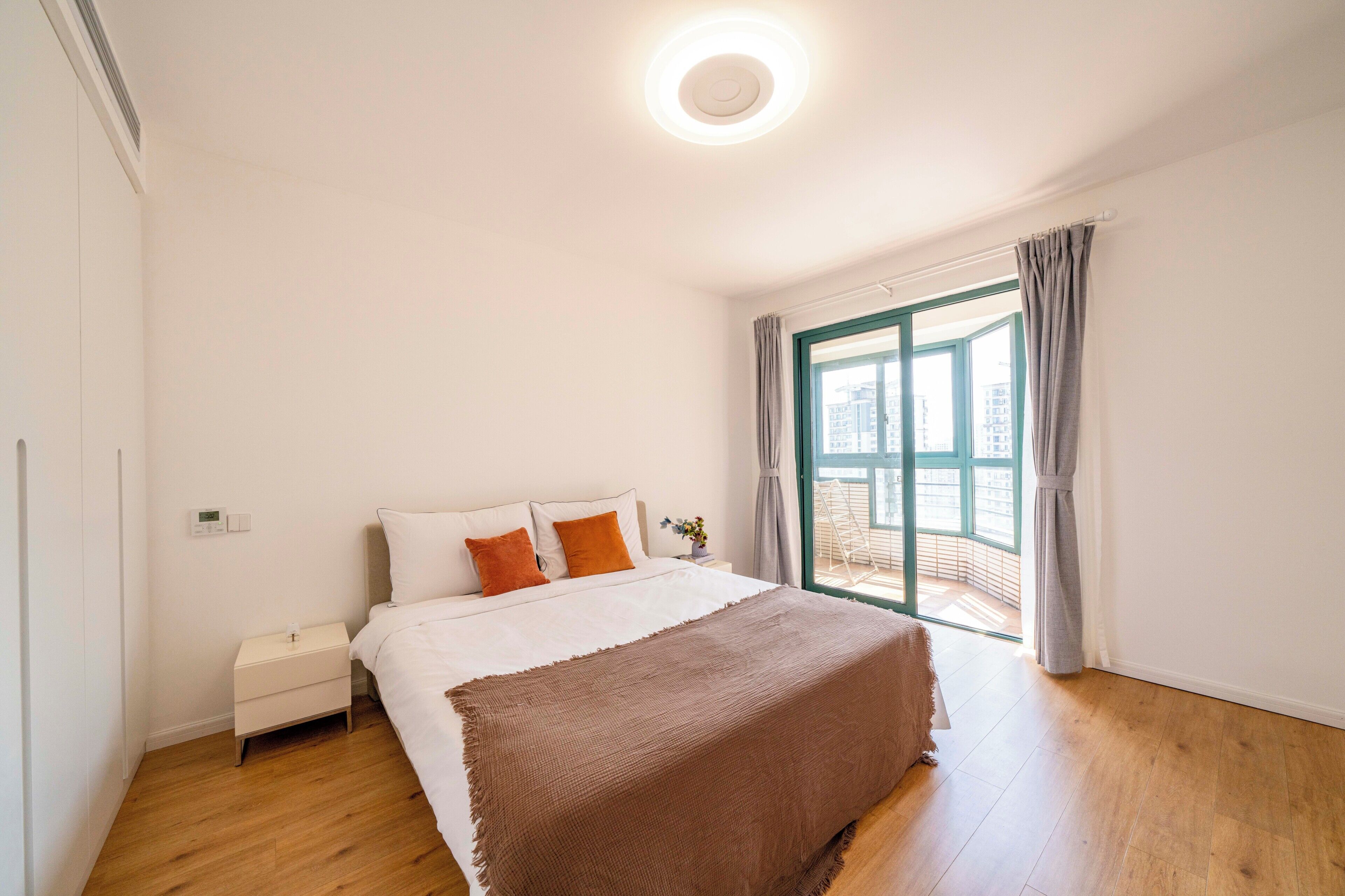 A bedroom with a bed, a nightstand, a window with curtains, and a view of the outside.
