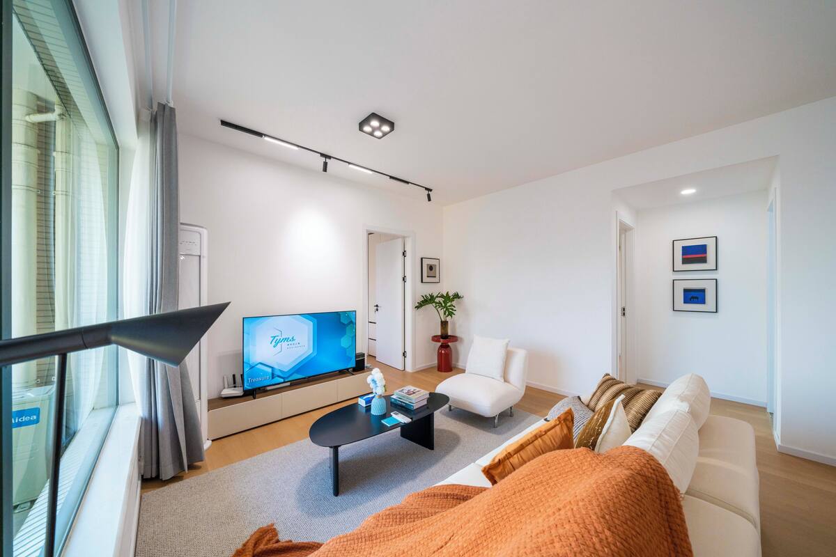 A modern living room with a flat-screen TV, a sofa, a coffee table, and a potted plant.
