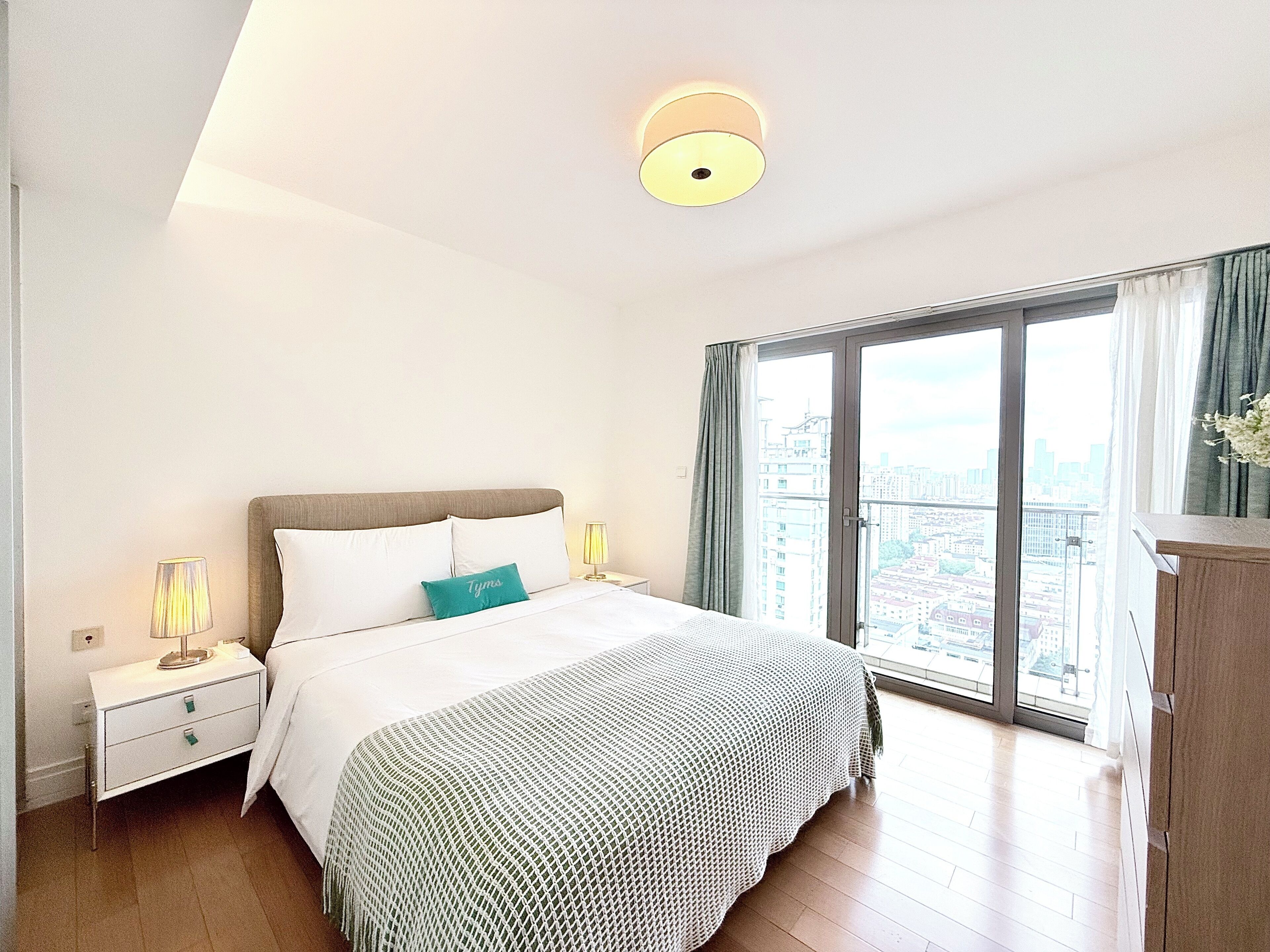 Una camera da letto moderna con un letto grande, un comodino, una lampada e vista sulla città attraverso un'ampia finestra.