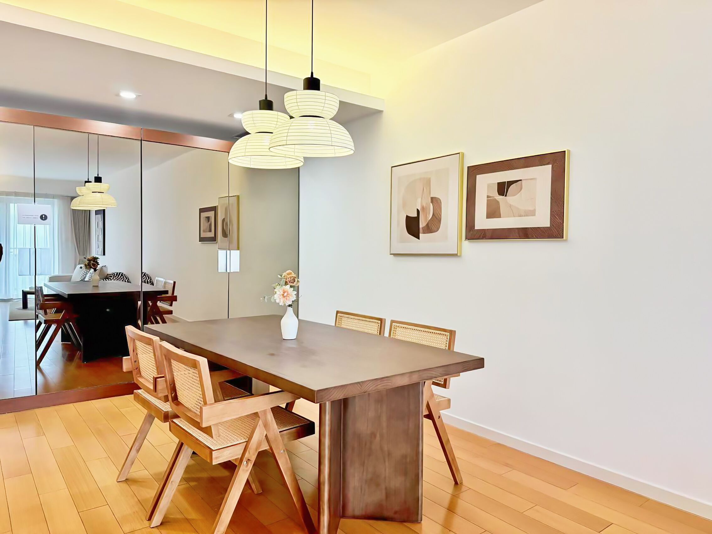 A modern dining area with a wooden table and chairs, pendant lighting, and framed artwork on the wall.