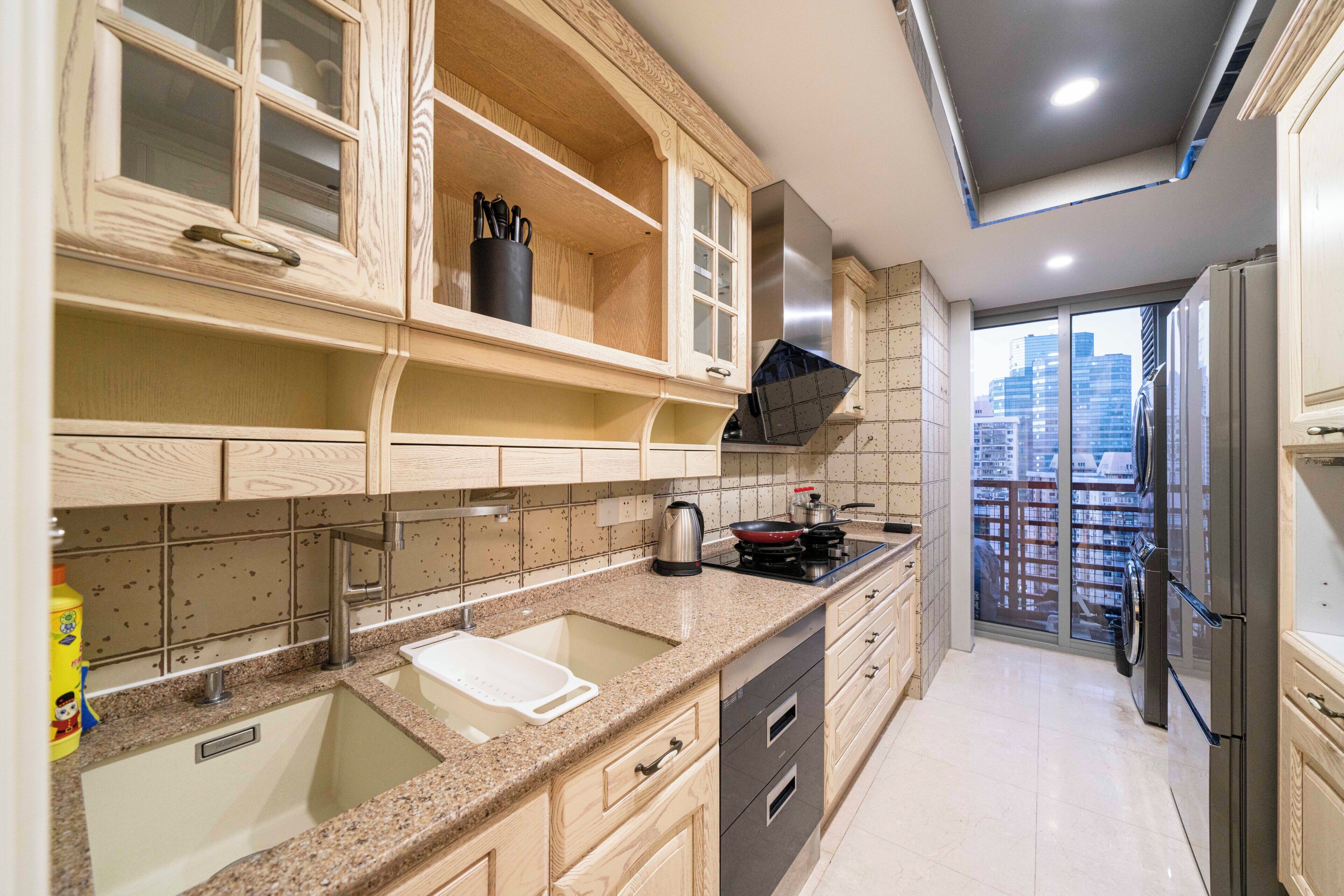 A kitchen with a double sink, stainless steel appliances, and a view of the city through a glass door.