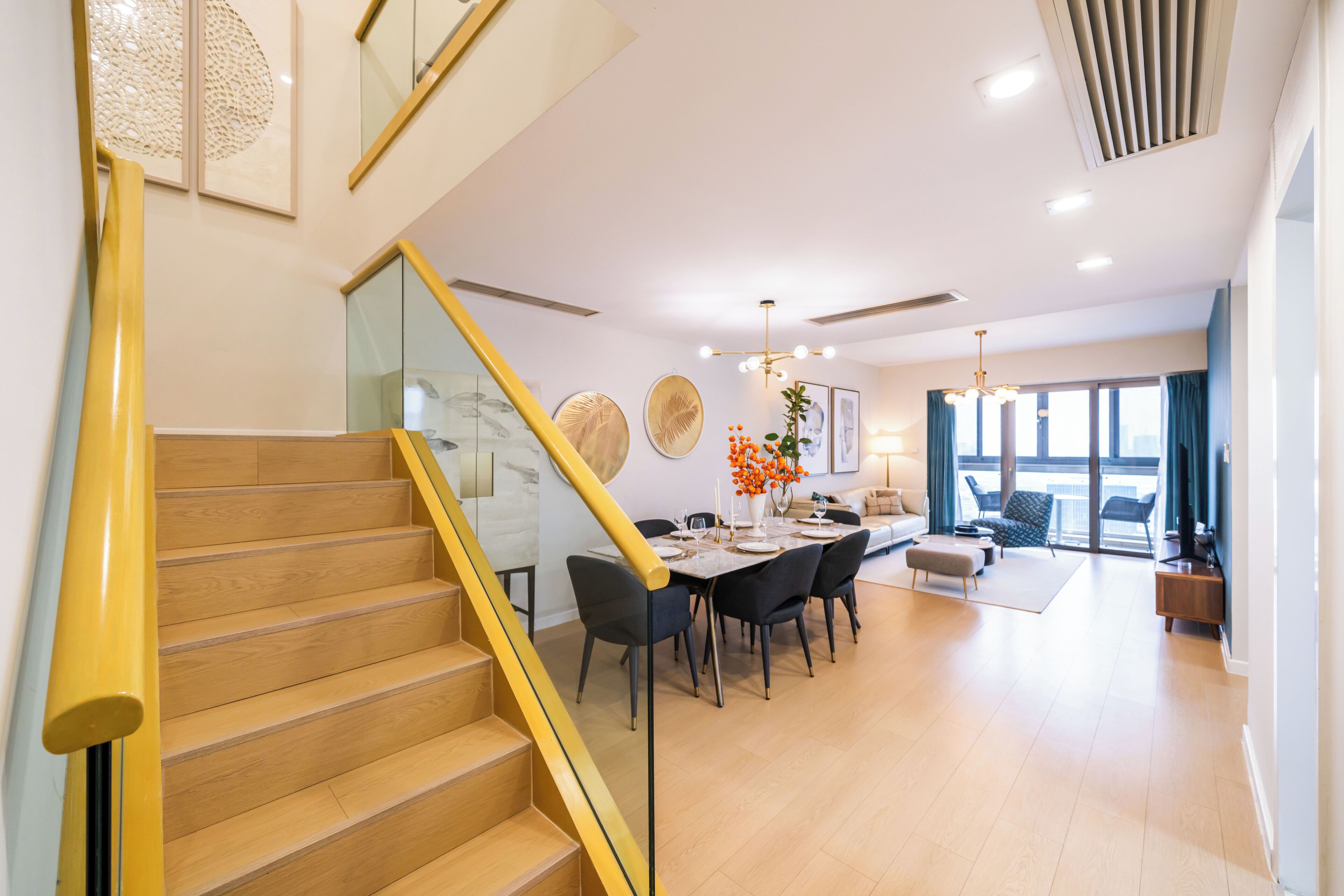 A modern interior with a wooden staircase, a dining area with a table and chairs, and a living space with a sofa and a TV.