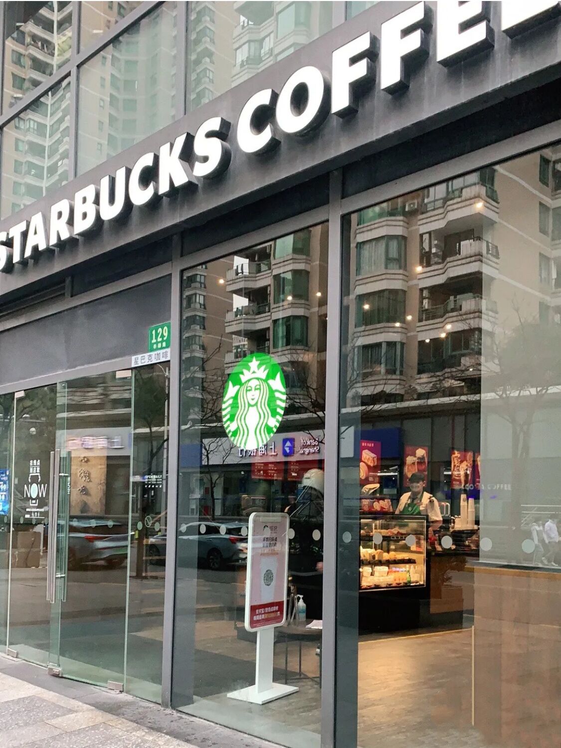 Una tienda Starbucks Coffee con un logotipo grande, escaparate de vidrio y un interior visible con productos de panadería.