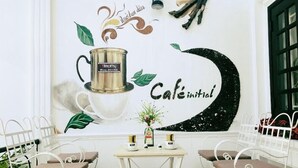 Interior d'una cafeteria amb un mural, dues cadires de metall blanc, una taula petita i una planta en test.