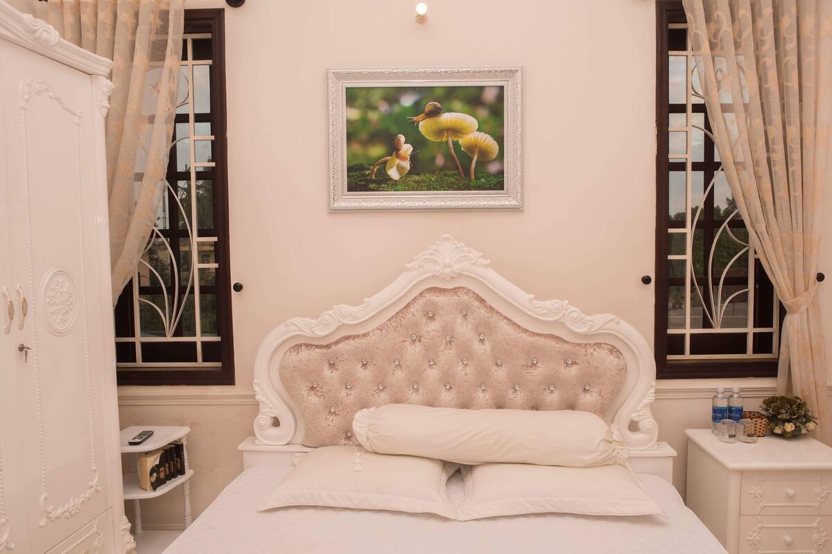A bedroom with a tufted headboard, a bedside table with a lamp, and a framed picture on the wall.