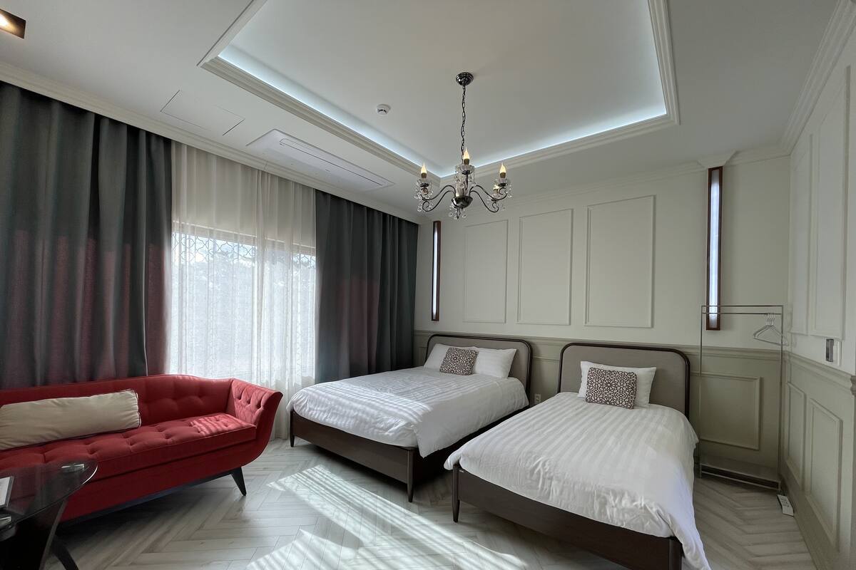 A hotel room with two beds, a red sofa, and a chandelier.