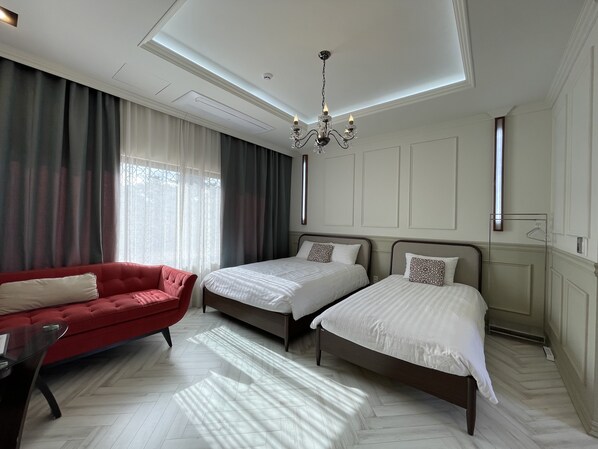 A hotel room with two beds, a red sofa, and a chandelier.