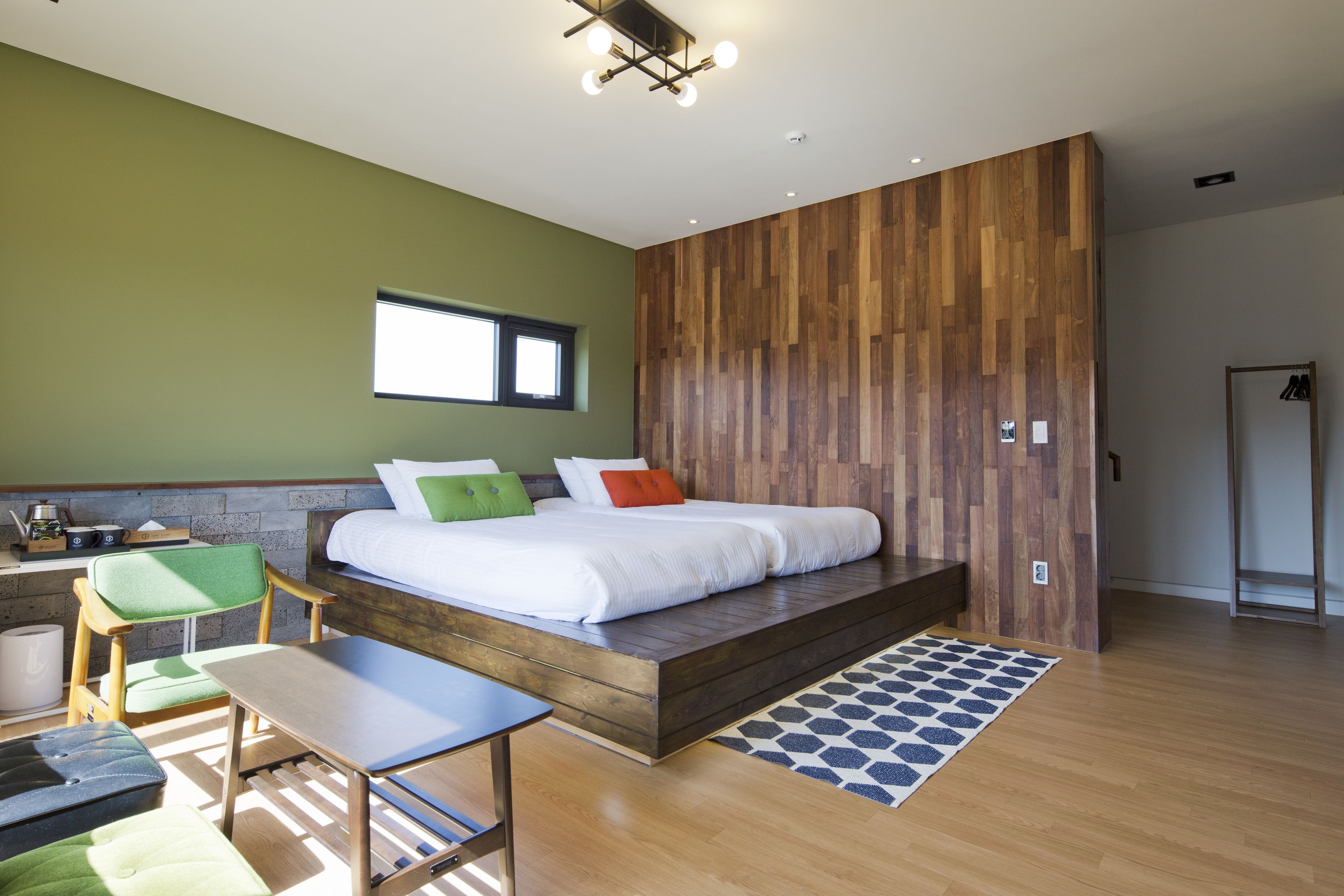 A modern bedroom with a wooden platform bed, a green chair, a small table, and a window.